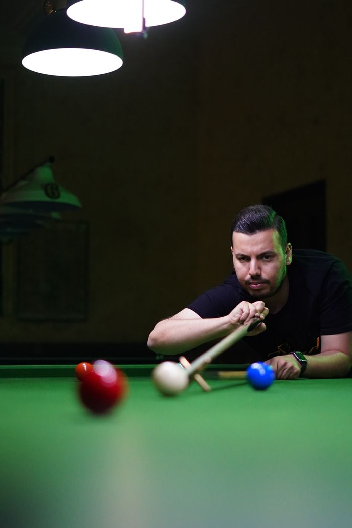 Man concentrating intensely as he lines up a shot in a snooker game indoors.