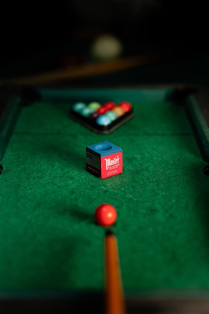 Focused view of a billiard table featuring red cue ball, chalk, and racked balls.
