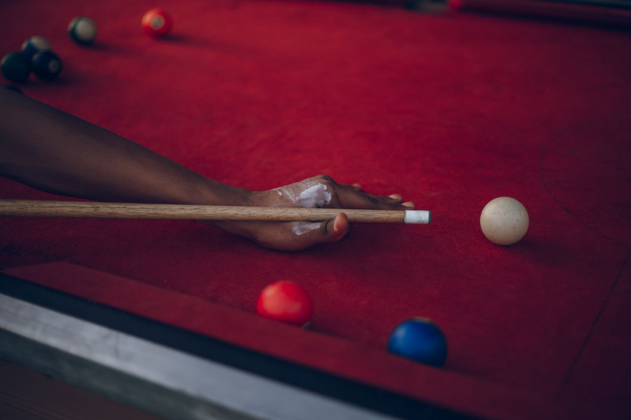 A person poised to play billiards on a red pool table, focusing on cue ball and colorful balls.