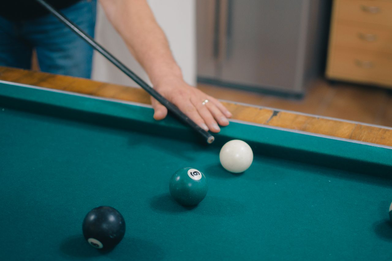 A player taking aim at a pool table with billiard balls and cue stick.