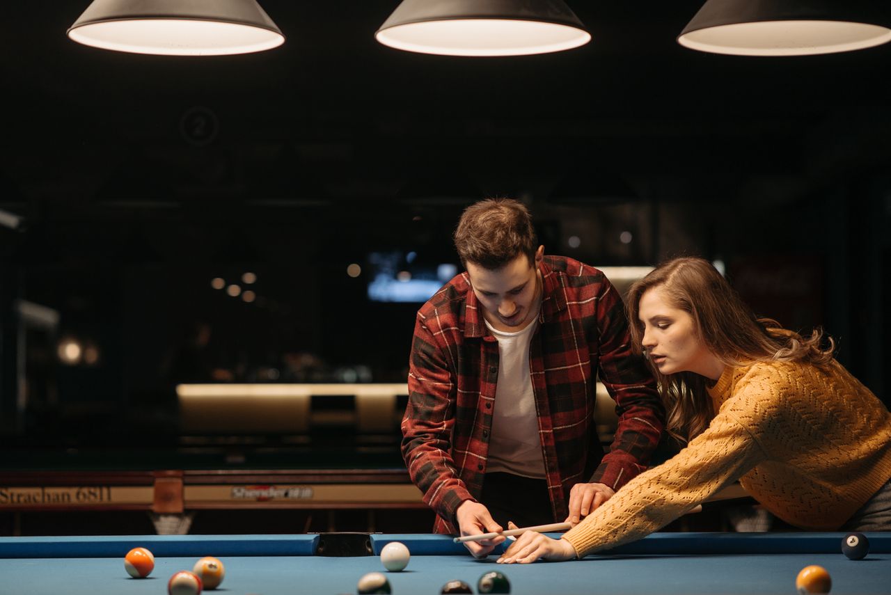 A young couple enjoys learning billiards together in a warmly lit room, sharing a recreational moment.