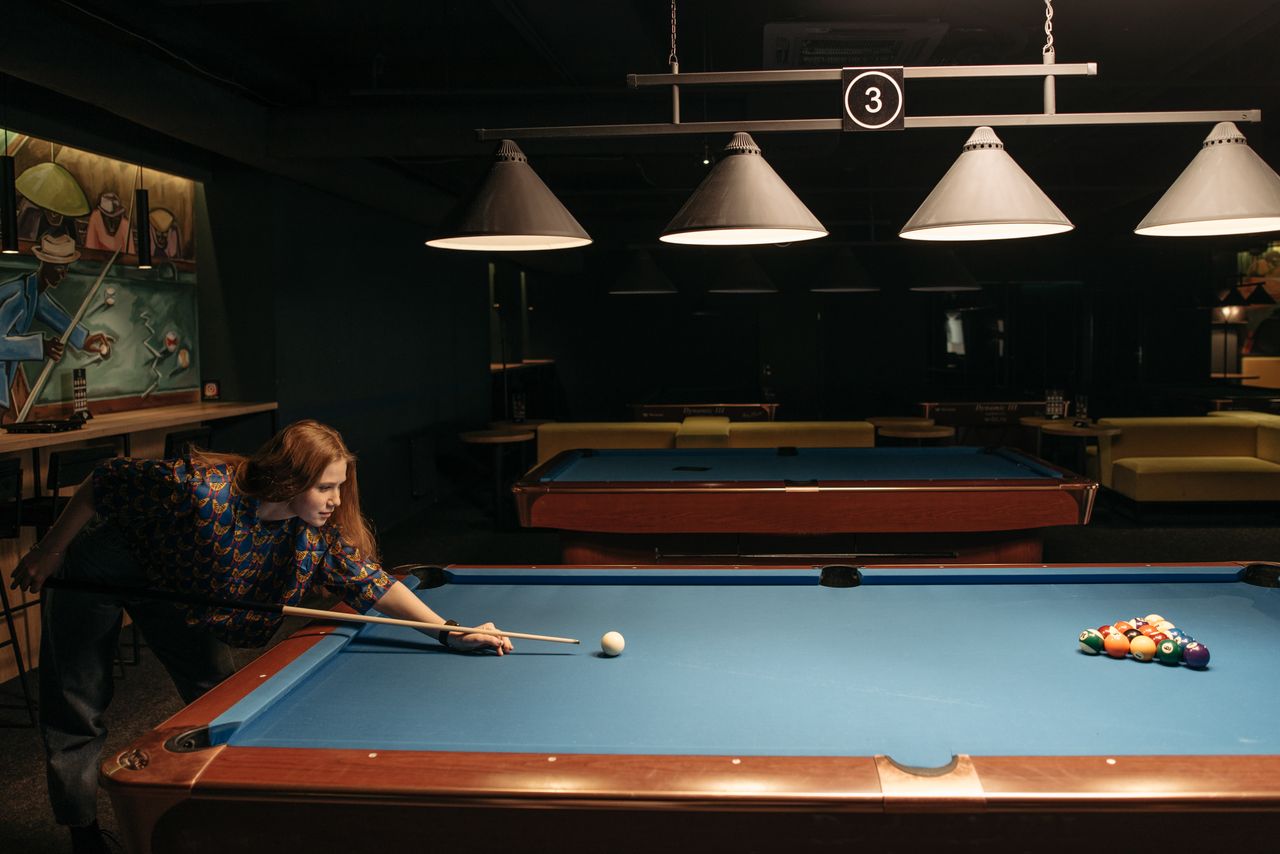 Woman enjoying a game of billiards in a dimly lit indoor setting, aiming at the balls.